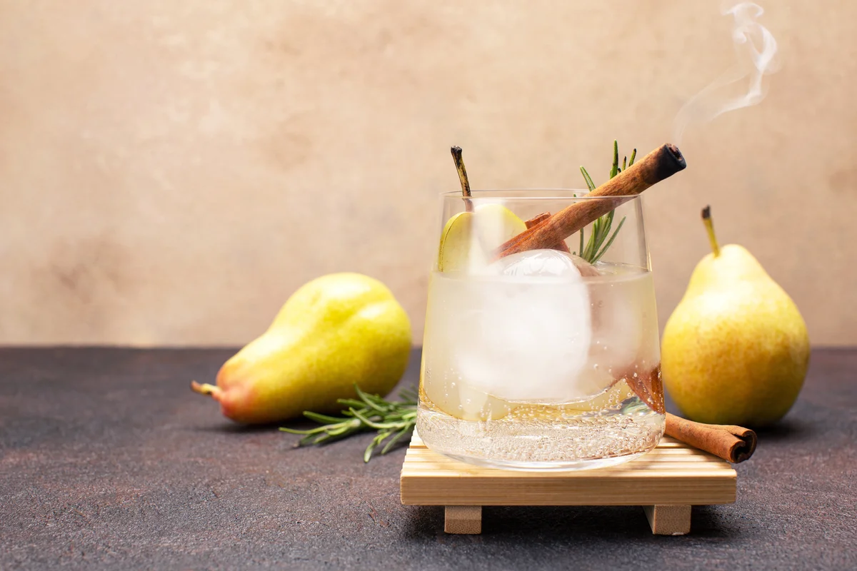 Refreshing pear cocktail with tonic, cinnamon and fresh rosemary on olive wooden board