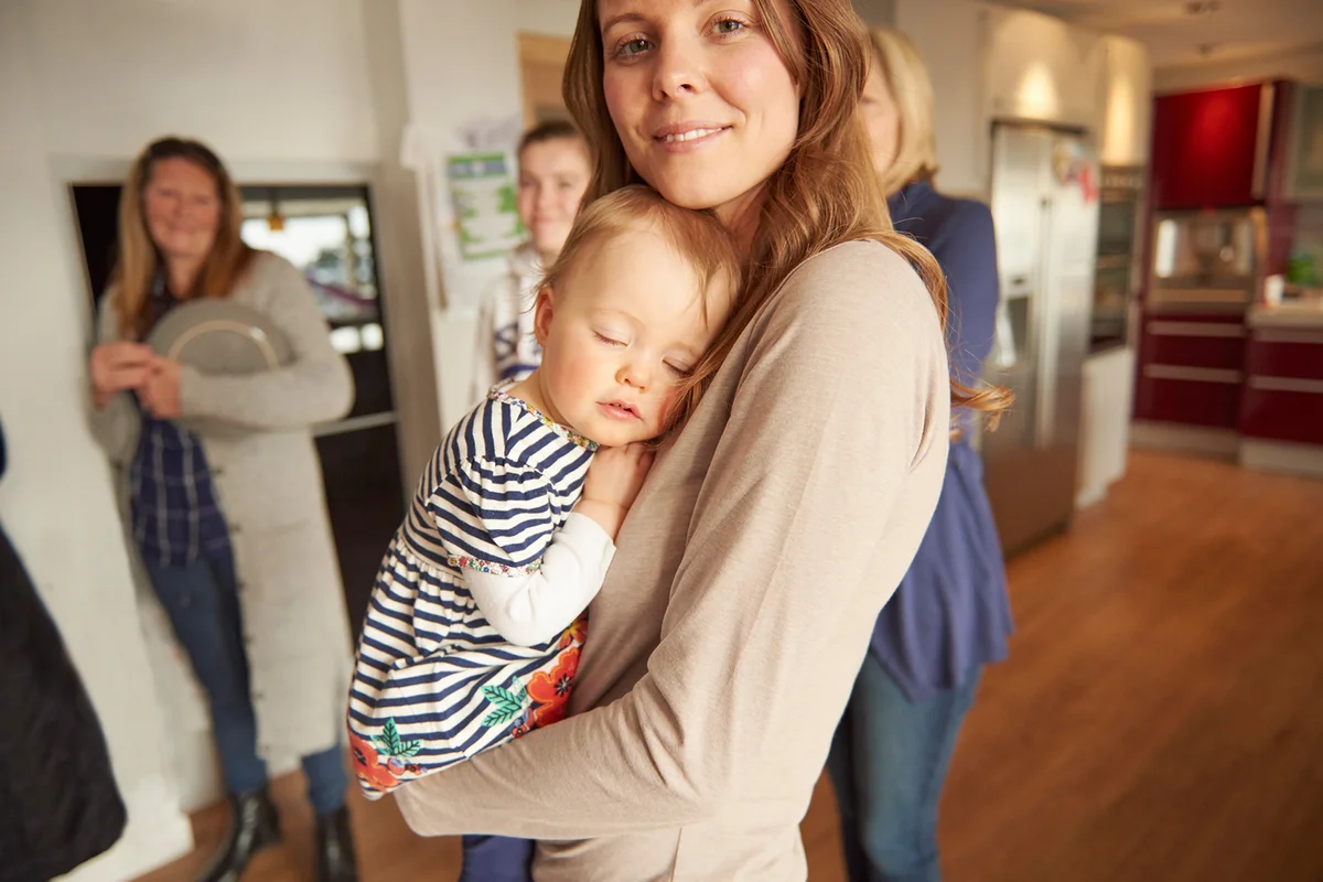 Portrait of young woman and sleeping baby daughter at family gathering