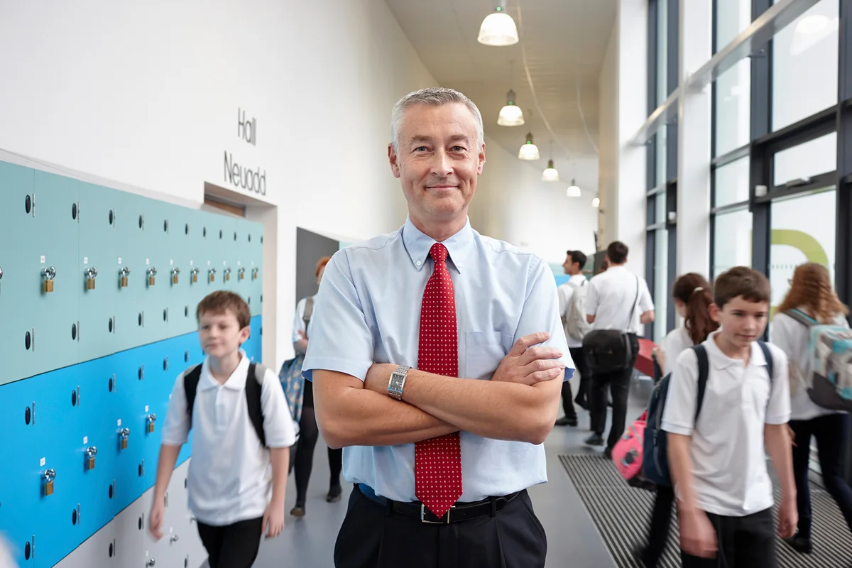 Portrait of male teacher with arms folded in school corridor