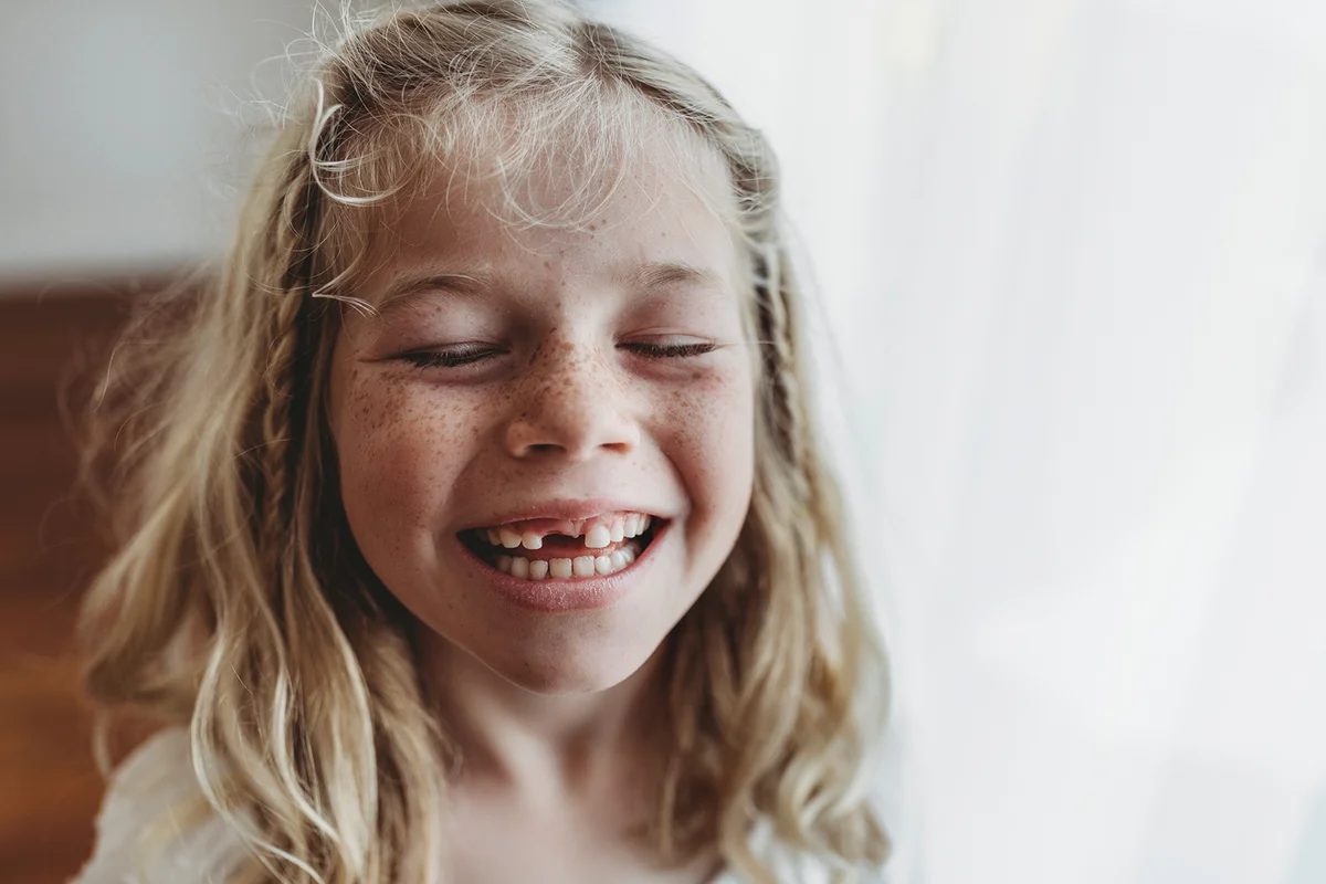 Portrait of young freckled smiling girl missing tooth with eyes closed