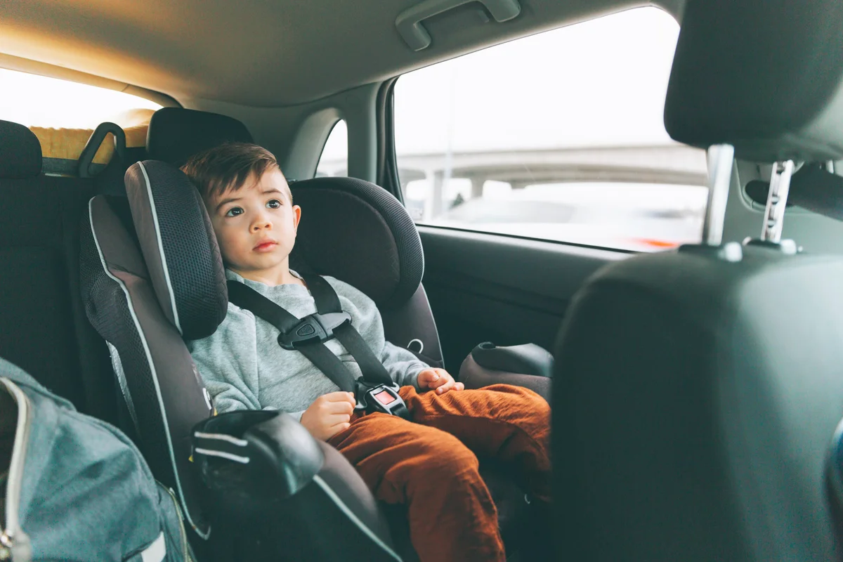 Little boy sitting in car on child's seat with fastened seat belt