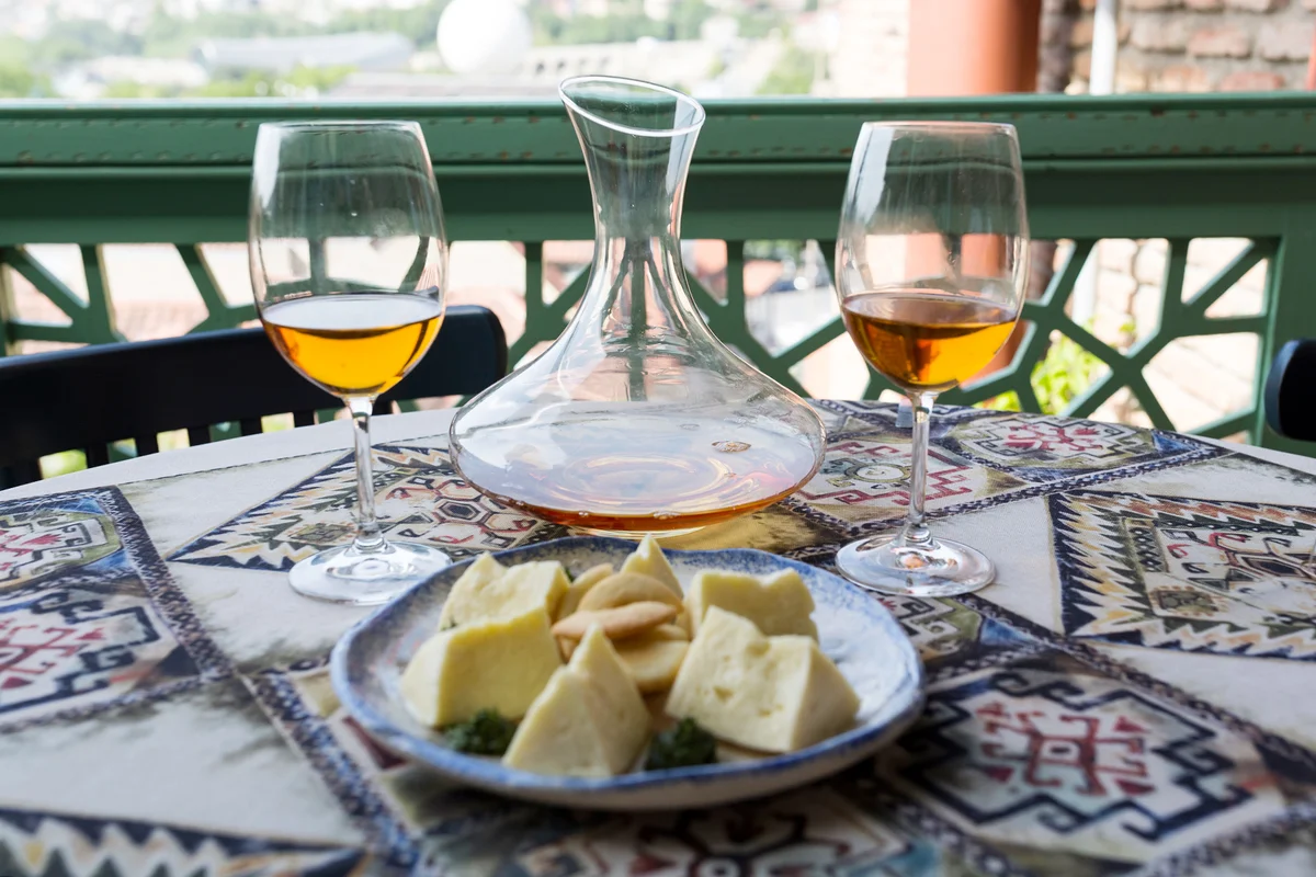 Two glasses and a jug, a decanter with orange qvevri wine. A plate with an assortment of Georgian cheeses