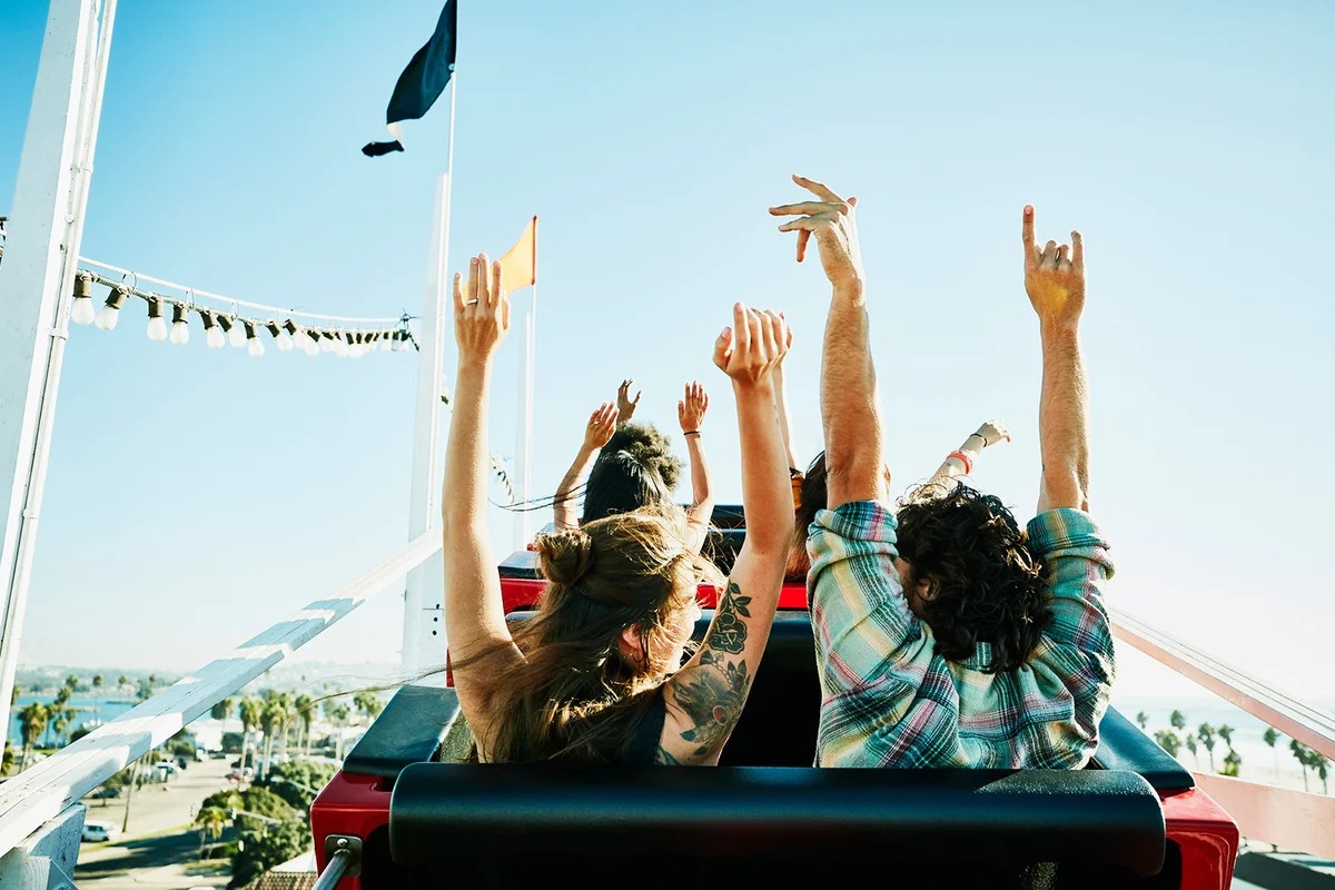 Couple with arms raised about to begin descent on roller coaster in amusement park