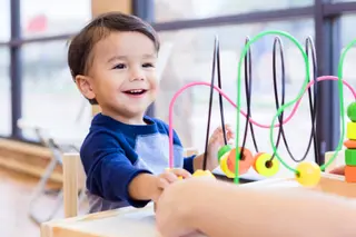 Toddler boy smiles while playing on the bead puzzle