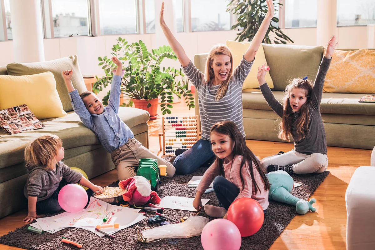 Young happy nanny having fun with small kids in the living room