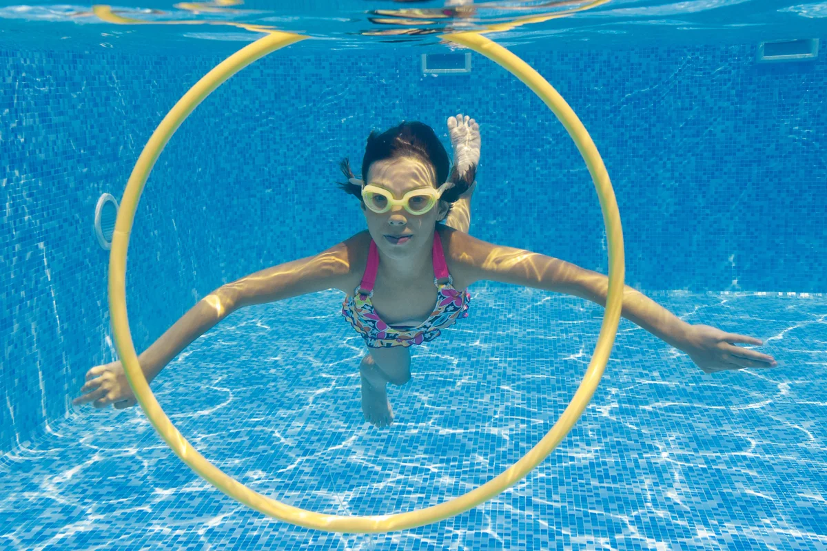 girl swimming under water in pool through hoop