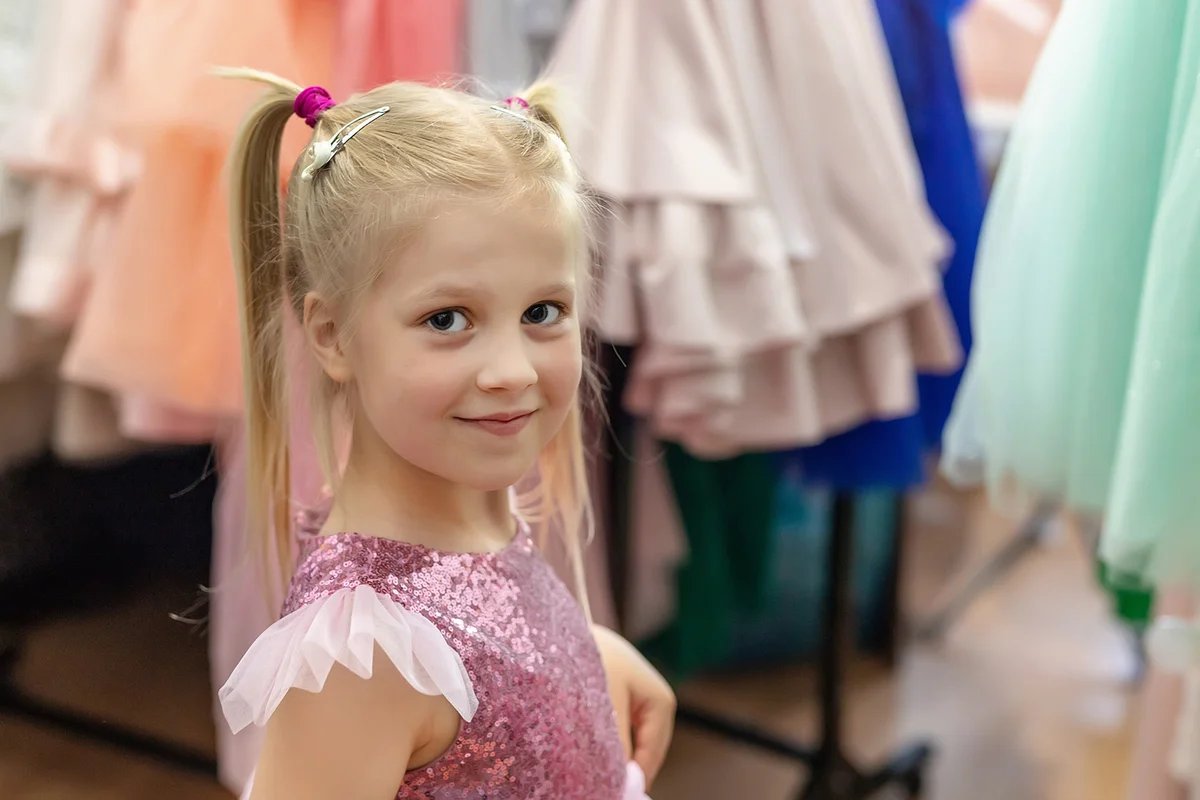 Little girl trying on fashion pink princess dress with sequins at children fashion