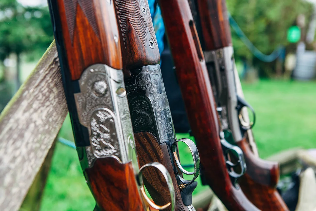 Various styles and types of sporting shotguns standing in a rack at a clay pigeon skeet shooting range