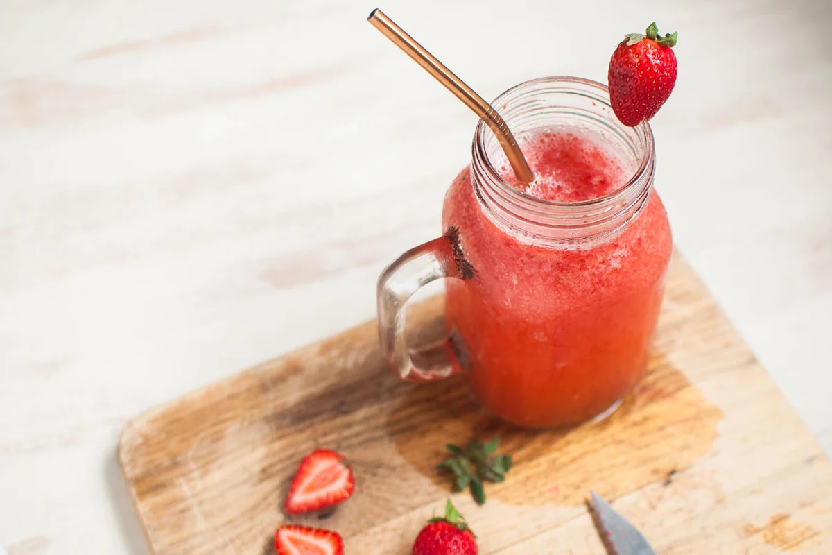 Strawberry smoothie with whole and sliced strawberries on a cutting board