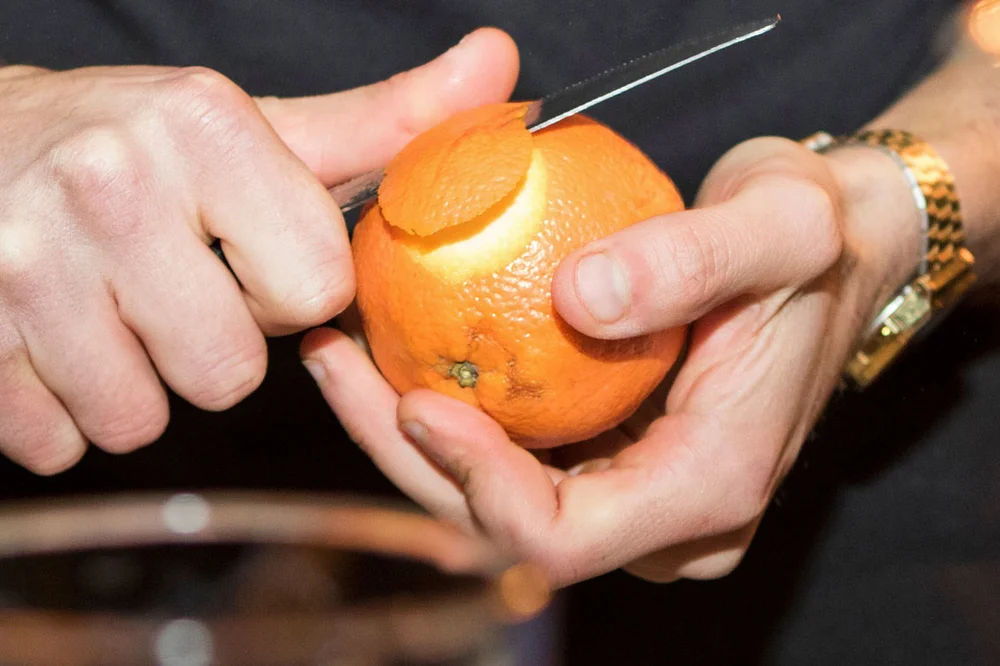 bartender peeling orange citrus coin for cocktail garnish
