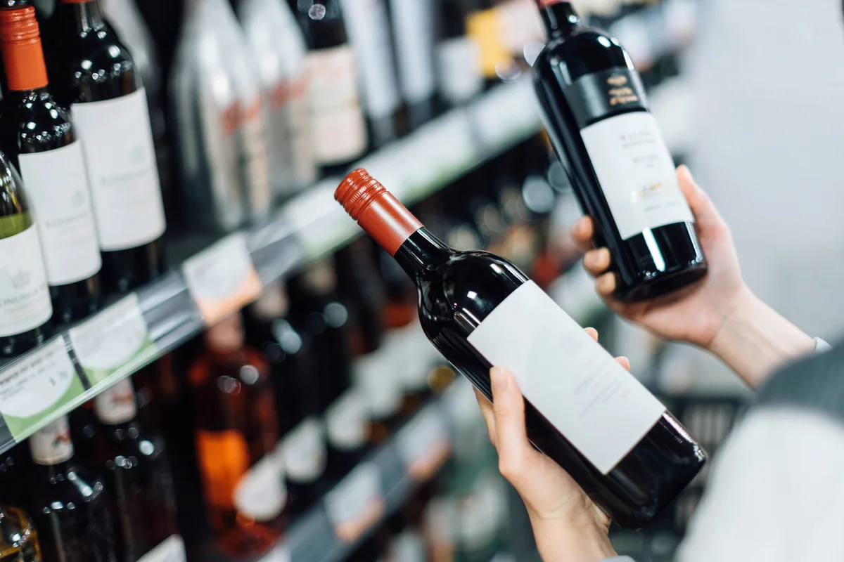 Woman walking through liquor aisle and choosing bottles of red wine from the shelf