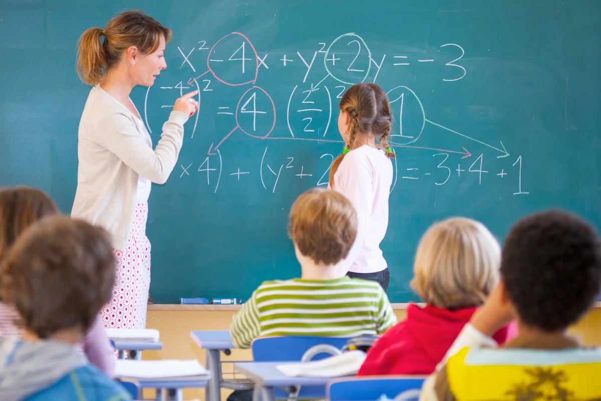 Primary school teacher explaining equation on classroom blackboard