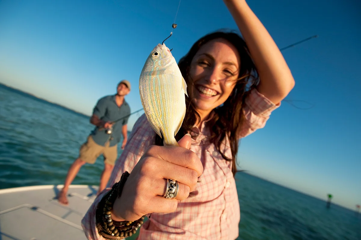 A woman smiles and holds up a small fish