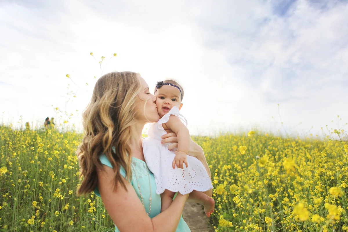 Mother kissing baby girl in field of flowers