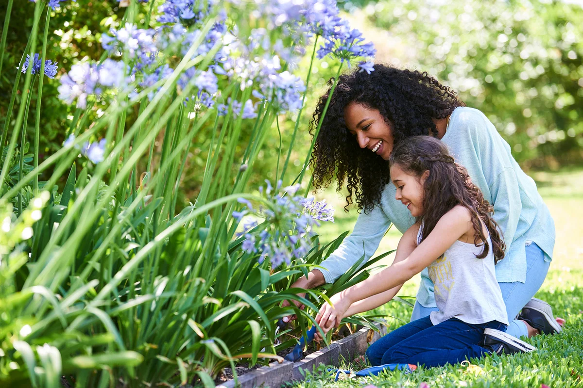 Mother and daughter planting flowers in garden