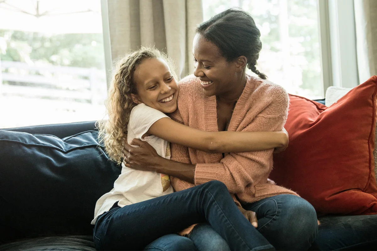 Mother hugging daughter on sofa