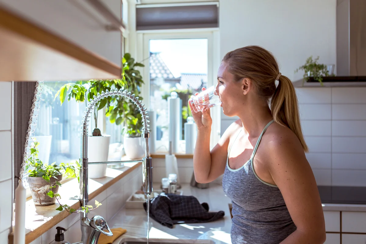 Woman in sports clothing drinking water at kitchen