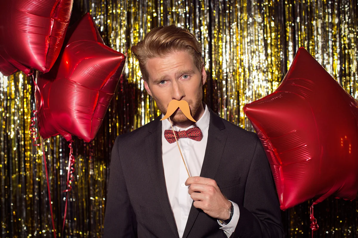 Young man wearing elegant black shirt celebrating or having party in front of fringe curtain