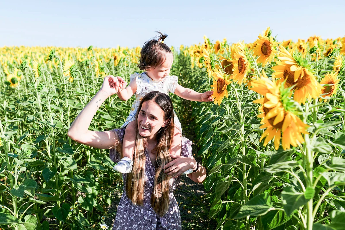 Mother with her daughter on her shoulders in the field of sunflowers