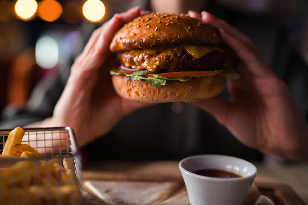 Hands holding an hamburger with french fries, sauce and beverage