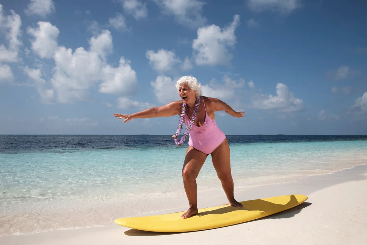 Senior woman standing on surfboard at the beach