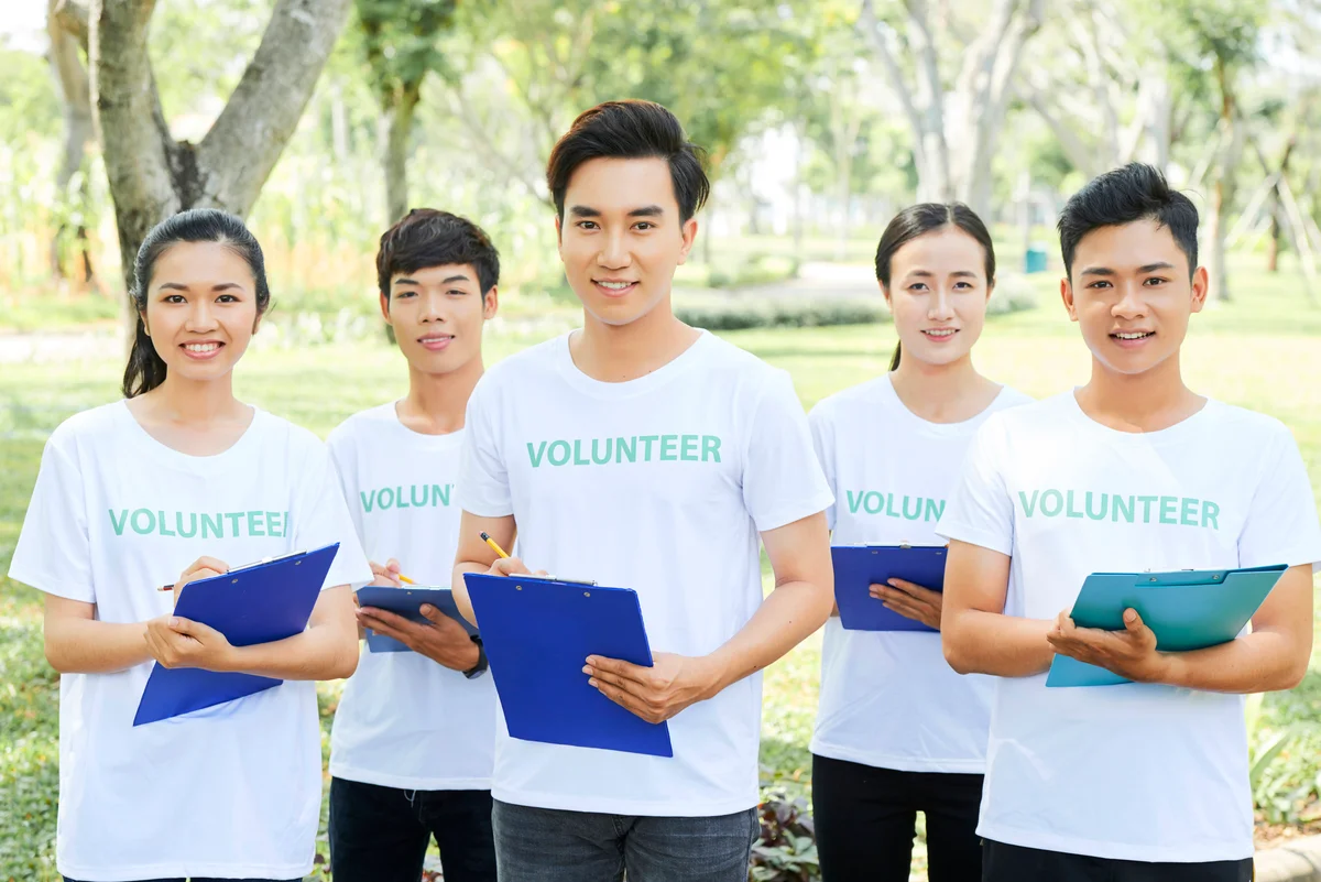 Group of volunteers with their leader standing in park with clipboard in hands