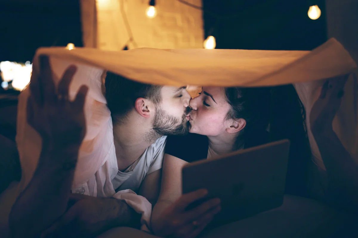 Couple using digital tablet in bed and kissing