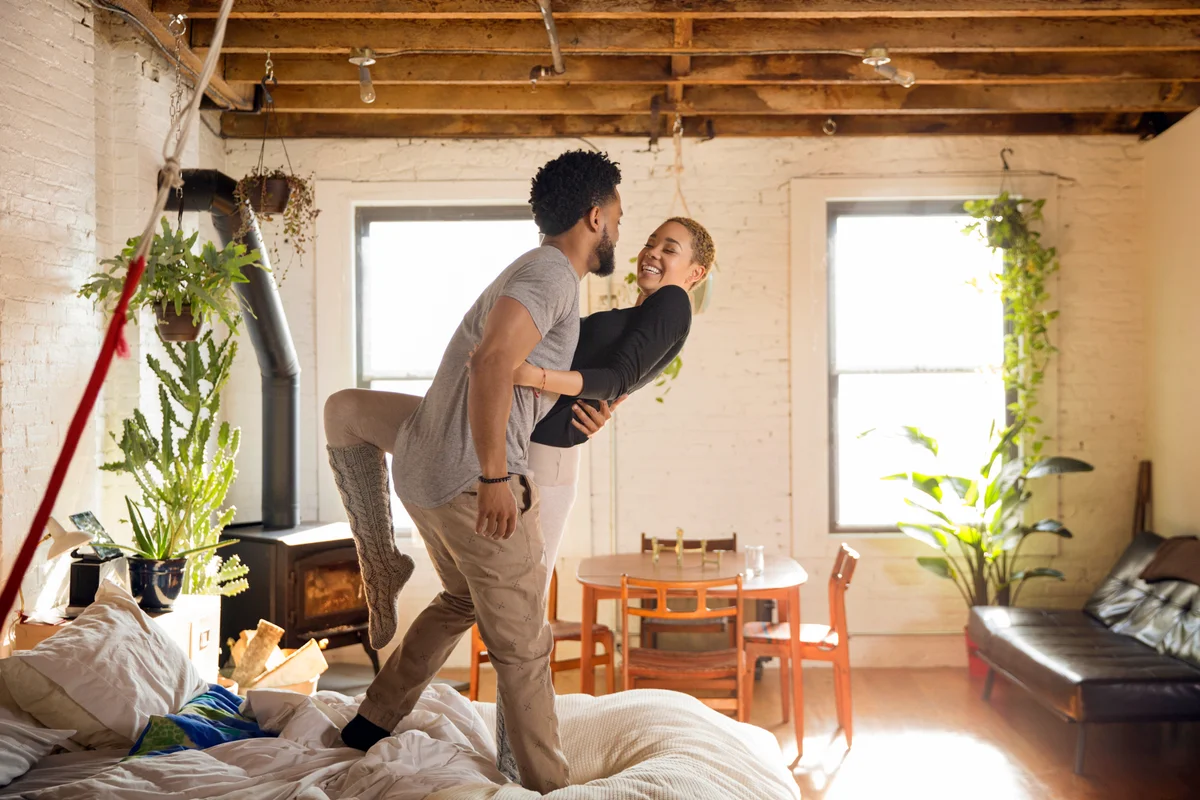 Cheerful couple dancing on bed at home