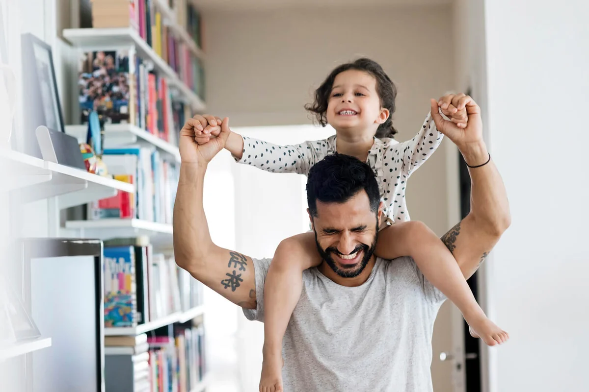 Happy father carrying girl on shoulder while standing at home
