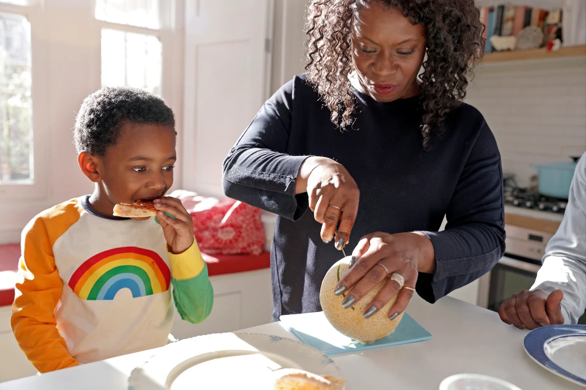 Mother cutting her young son some melon at home in the kitchen
