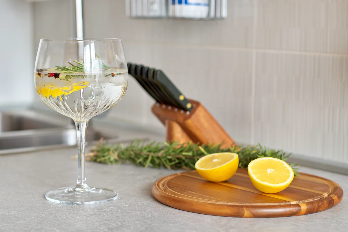 Preparing Gin And Tonic With Lemon And Rosemary In Crystal Glass On Kitchen Desk