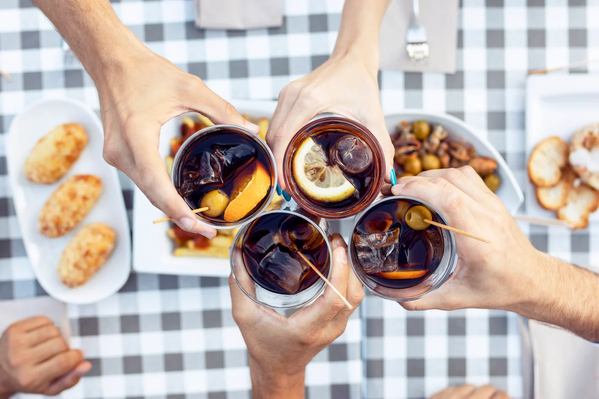 Hands of friends toasting vermouth at table in cafe