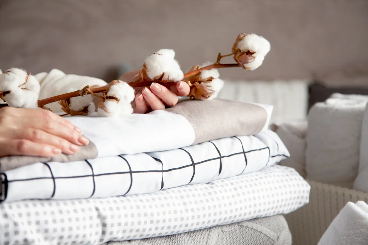 Woman hands holding the cotton branch with pile of folded bed sheets and blankets