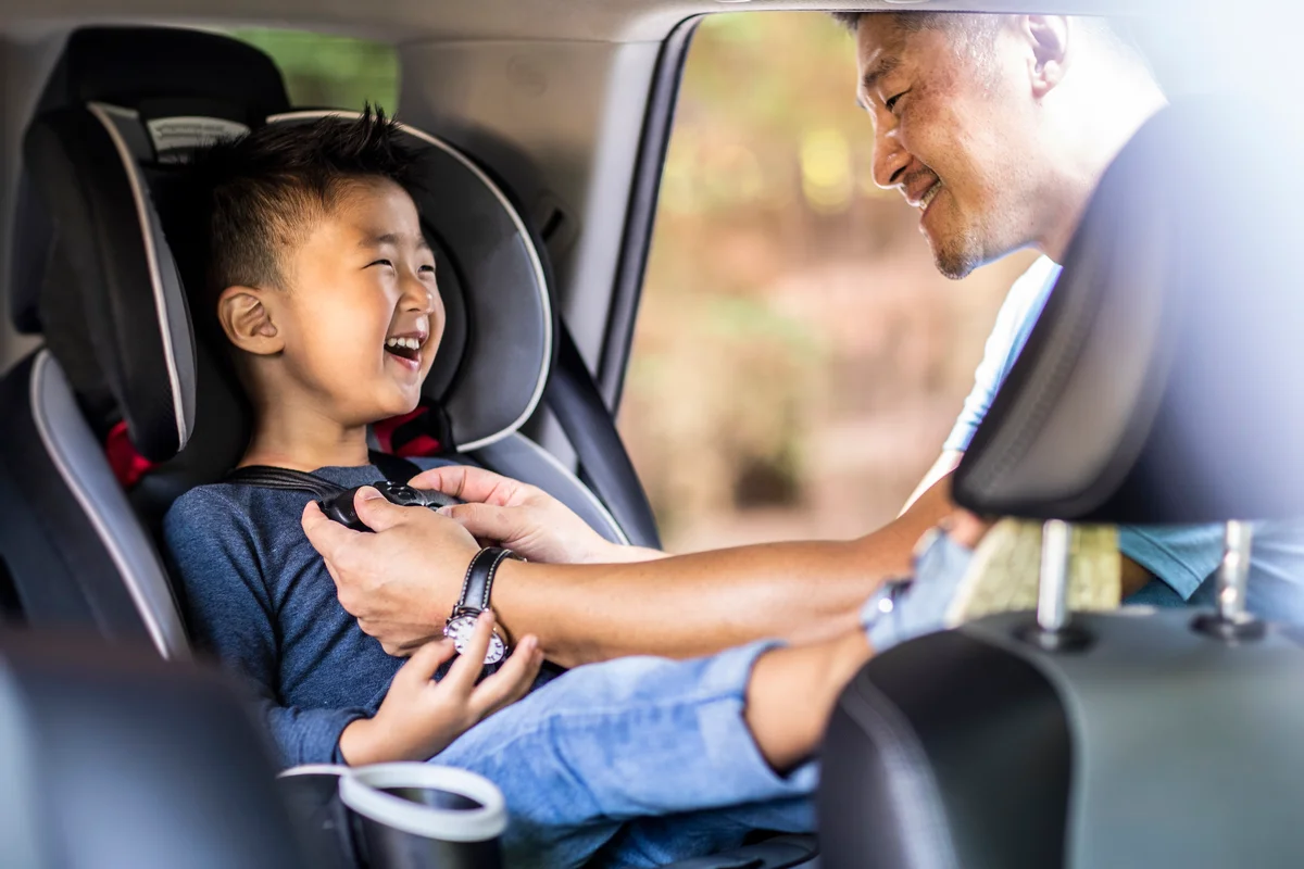 Father buckling son in car seat