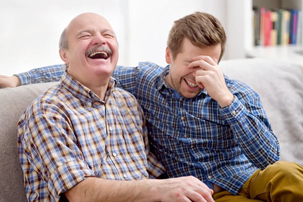 Father and son are sitting on the sofa in the living room and remember joke