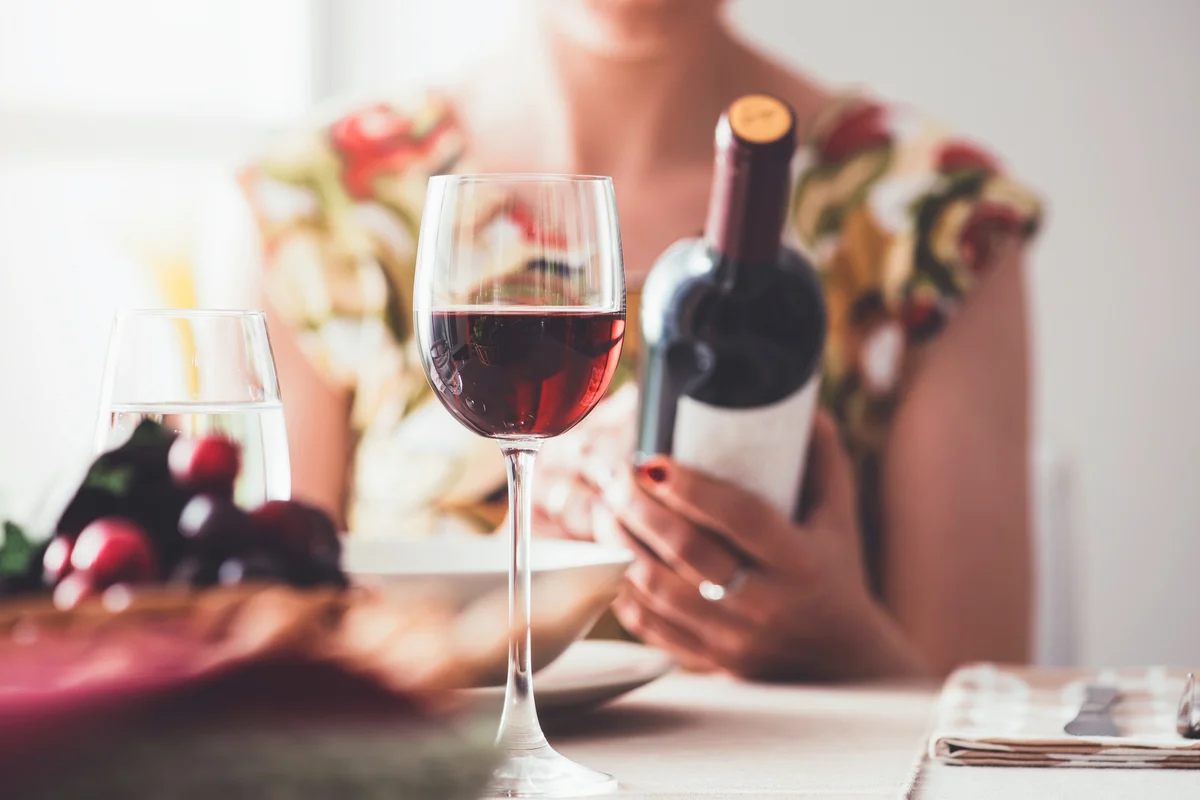 Woman having lunch at the restaurant and reading a wine label on the bottle