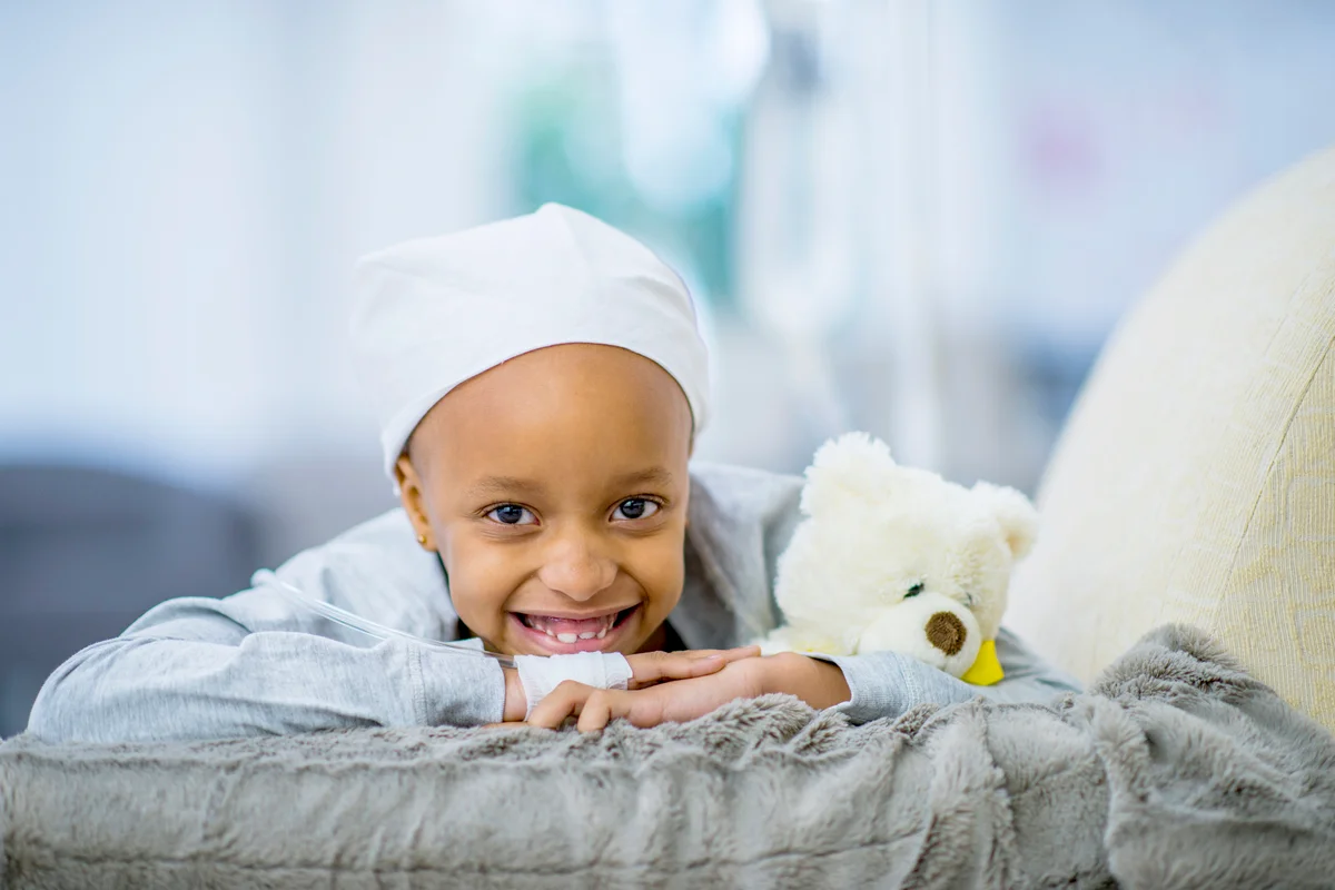 Smiling girl with cancer holding a teddy bear