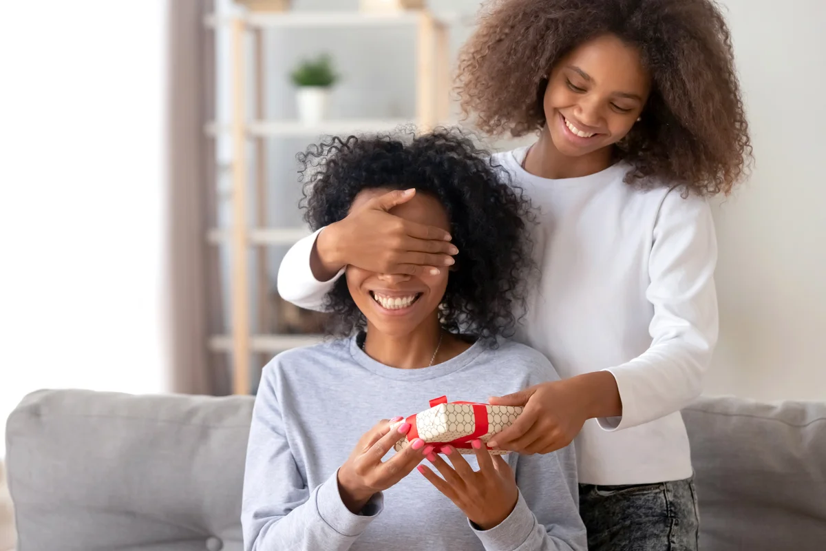 Happy teen girl closing her mother's eyes to surprise her with gift