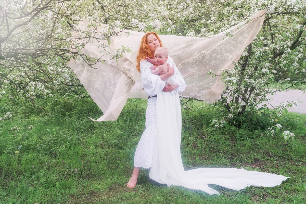 Woman With Baby Son Standing Against The Blooming Tree