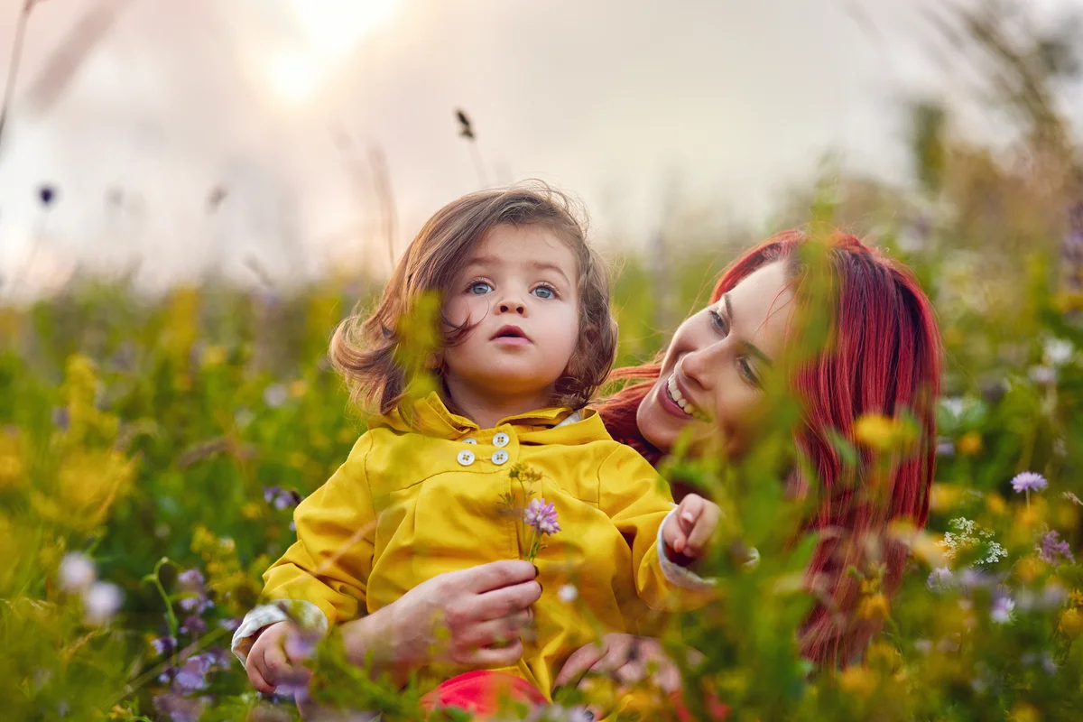 Red haired mother with little daughter sitting in garden of plants and flowers
