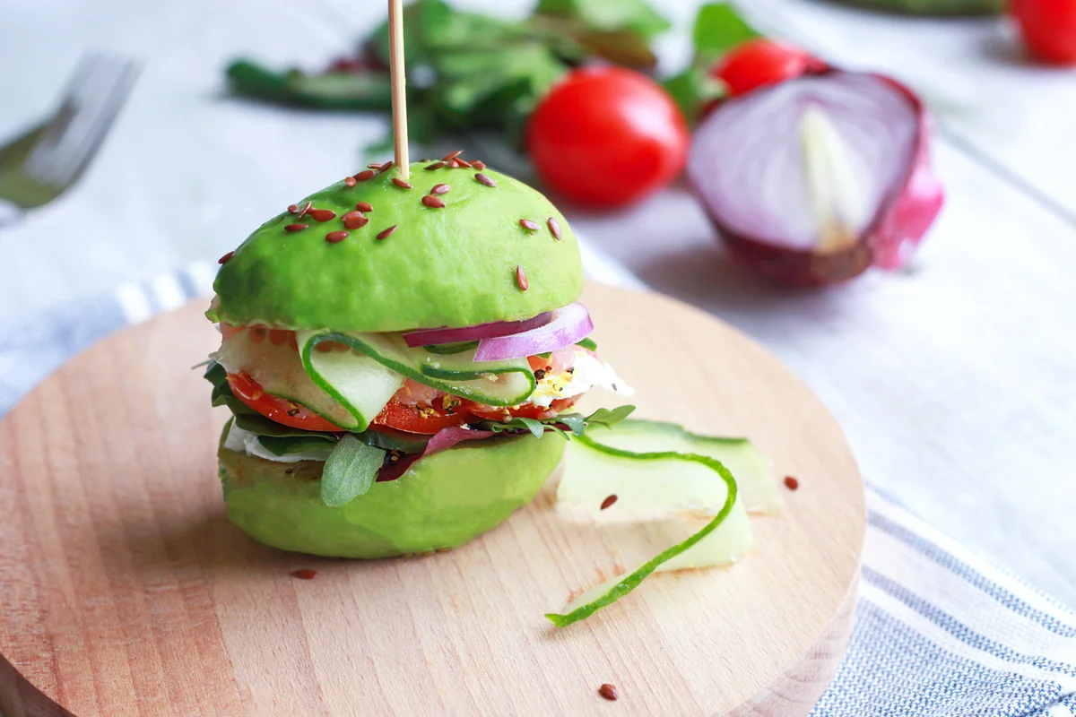 Avocado burger with cucumber, tomato, onion, greens and seeds on wooden plate