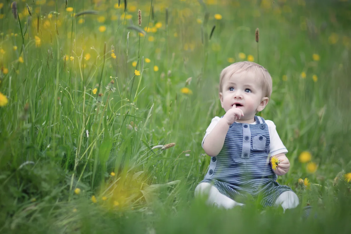Cute baby sitting in flowery meadow in spring