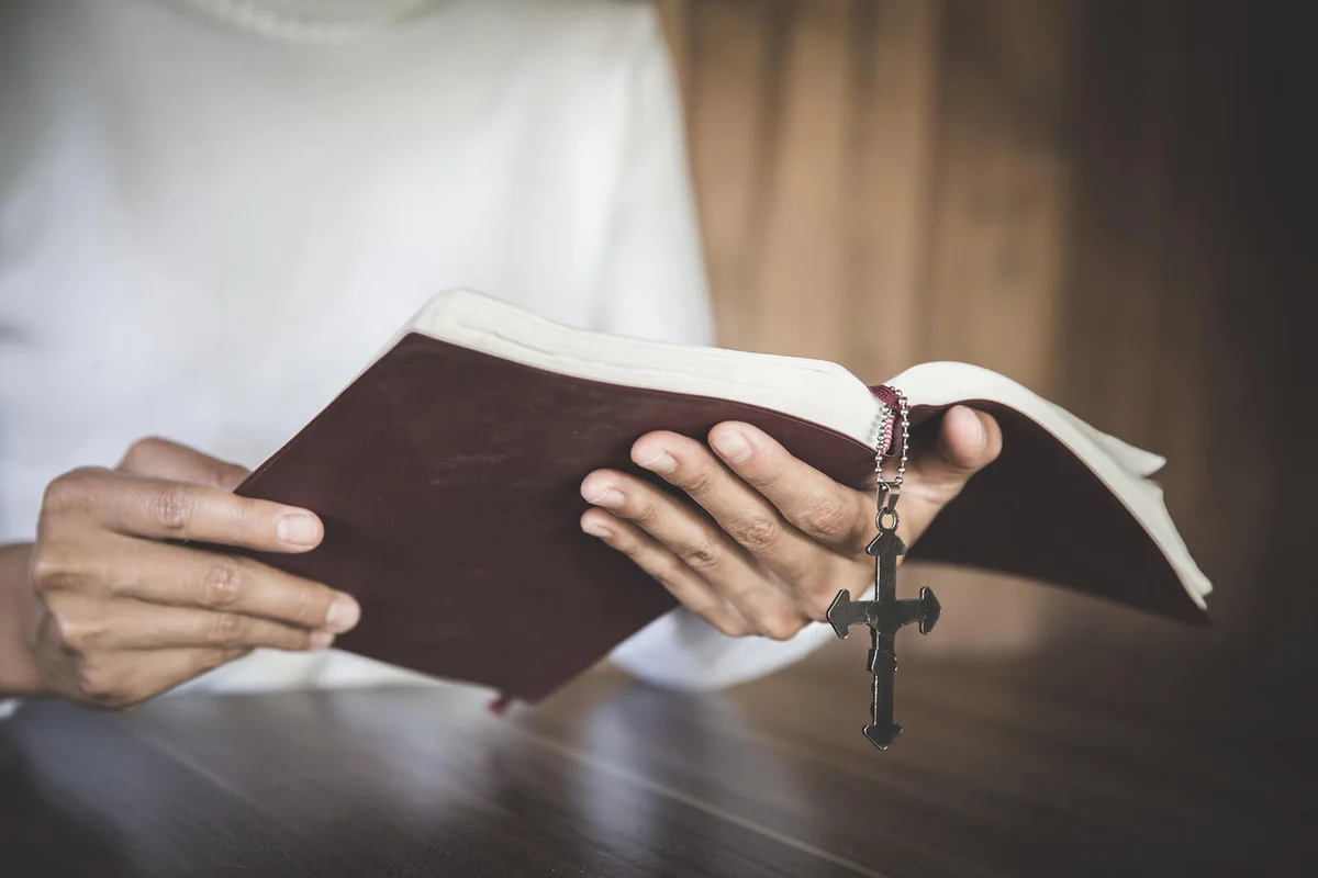Human hand holds cross and bible