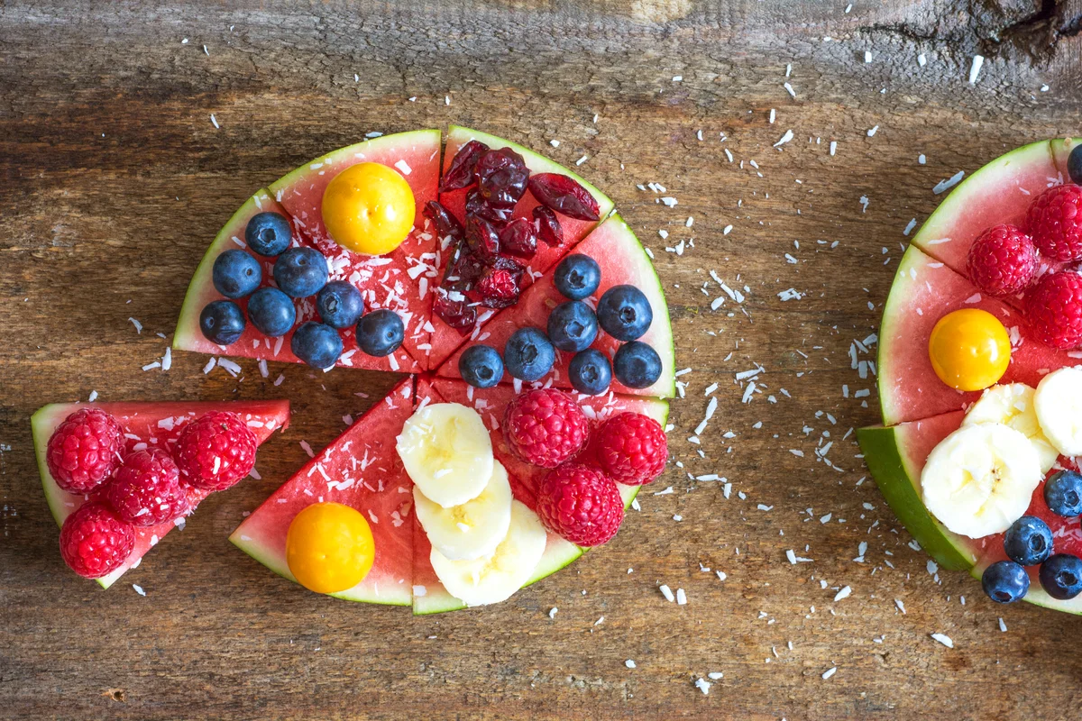 Fruitcake made of watermelon garnished with various fruits sprinkled with coconut flakes