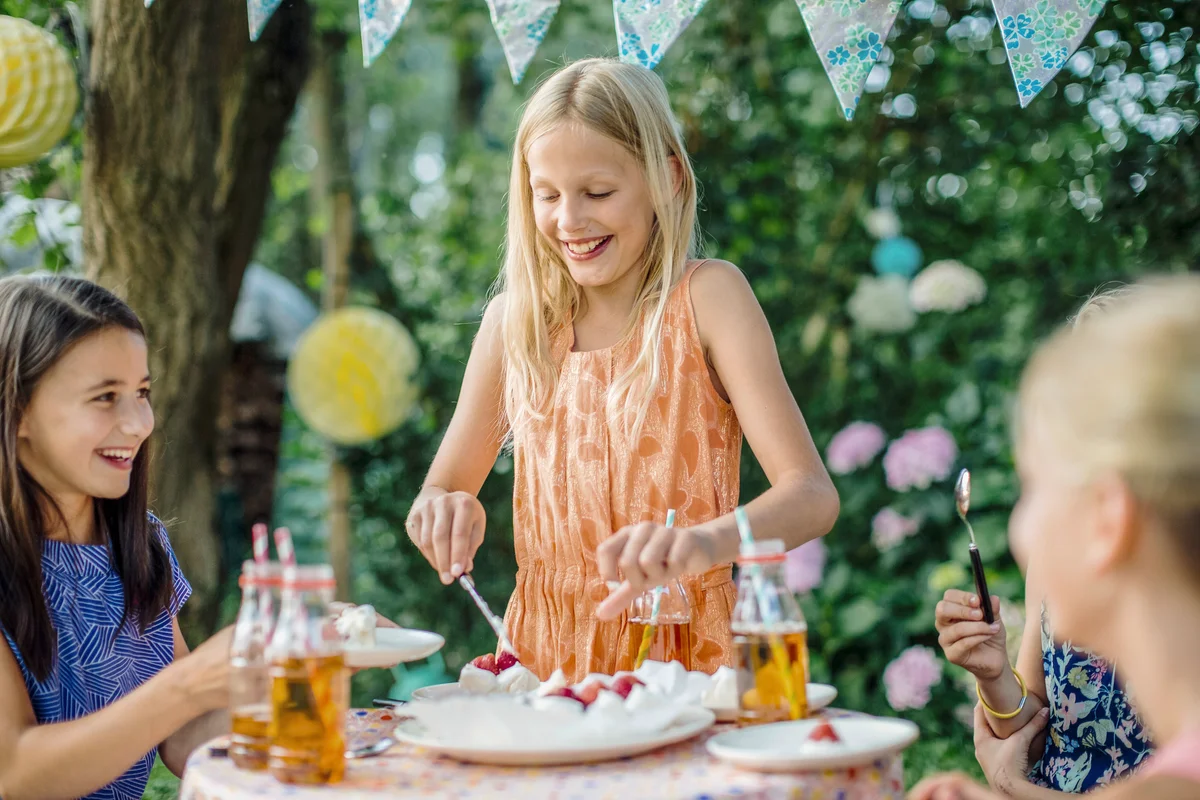 Girl dishing up cake on a birthday party outdoors