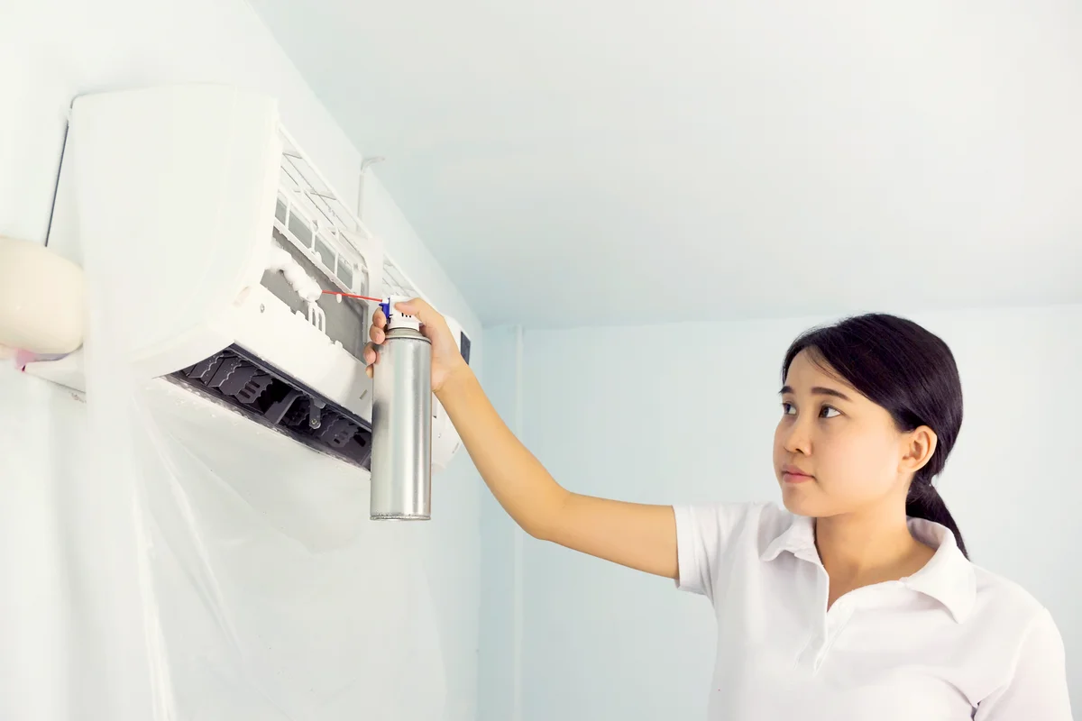 Woman cleaning air conditioner by foam cleaning agent