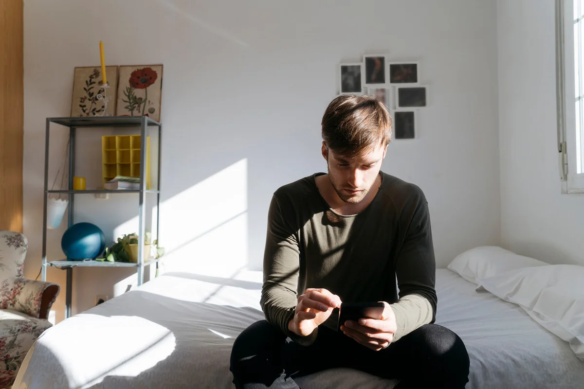 Young man sitting on bed looking at his smartphone
