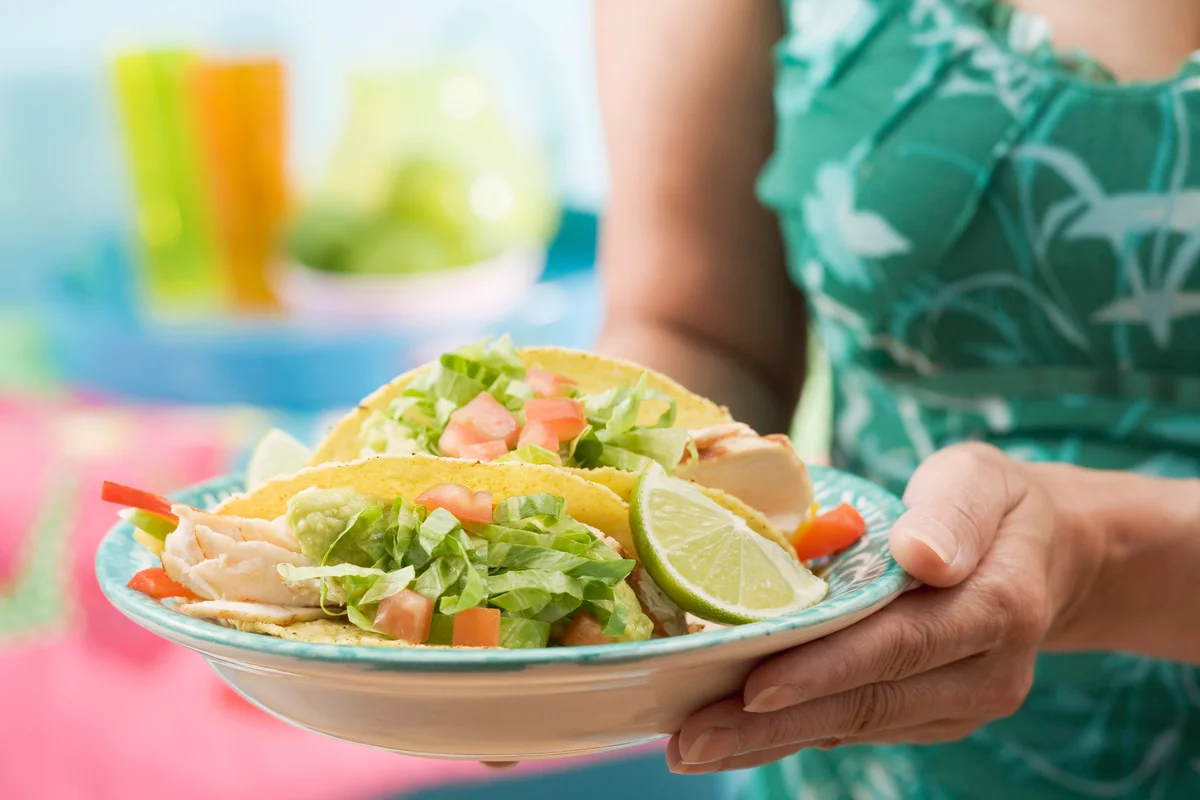 Woman holding plate with two chicken tacos
