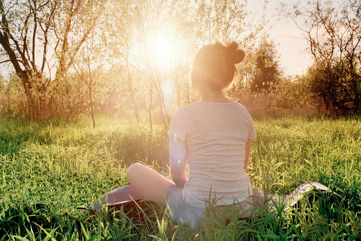 woman sitting in grass field facing sun rebirth ritual