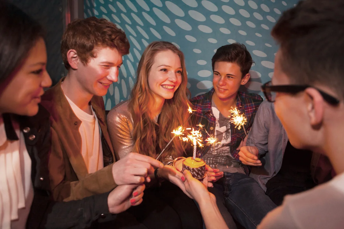 Group of teenagers sitting around birthday cake with sparklers